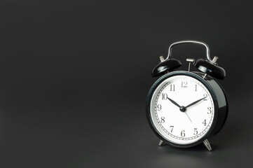 Black vintage alarm clock with white dial on black background flat lay copy space. Retro clock, mechanical alarm clock. Minimalistic background, concept of time, deadline, time to work, morning