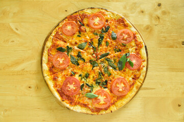 Homemade pizza with cheese and tomatoes and basil on a wooden table with copy space.