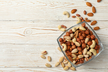 Bowl with different nuts on white wooden background