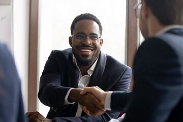 African Caucasian businessmen in formal suits express respect shake hands start negotiations. Common project growth sales increase, partnership, business etiquette, leadership, racial equality concept