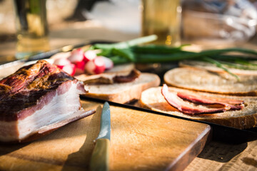 Bacon and knife on a wooden desk. Grilled bacon slice on fatty bread, green onion and fresh radish in the background on a hungarian summer grill party. Barbeque background