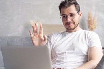Happy young man video chatting on laptop computer while sitting on the sofa at home