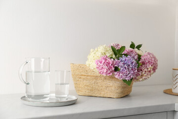 Obraz na płótnie Canvas Beautiful hydrangea flowers in basket and water on light table