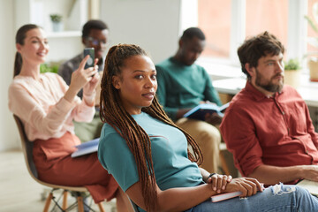 Multi-ethnic group of people sitting in audience during training seminar or business conference in office, focus on African-American woman looking at camera in foreground, copy space