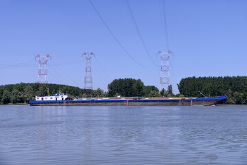 Fototapeta na wymiar Cargo ship on the river and electric pylons in the background