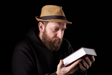 a white bearded man in a hat tenderly holds a thick book in his hands