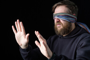 a bearded white man with a blindfold on his eyes fumbles for something
