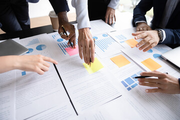 Close up table full of papers, diverse businesspeople analyzing report in charts and graphs discuss...