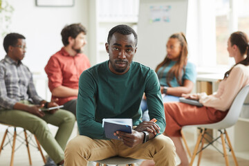 Multi-ethnic group of people sitting in circle while discussing business project in office, focus on African-American man looking at camera in foreground, copy space