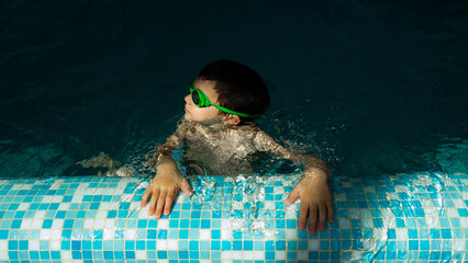 Boy in swimming glasses bathes in the pool