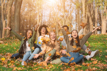 Group of cheerful friends playing with autumn leaves in park