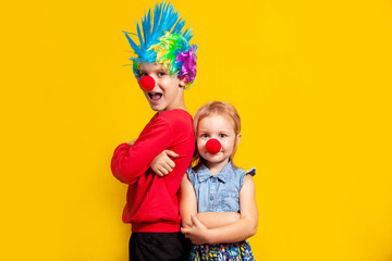 boy in a clown costume, a wig and a bright nose, the concept of a holiday and fun on a yellow background in the studio, a portrait to the waist