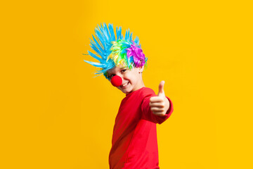 Boy clown with red nose and wig on a yellow background, portrait by belt, yellow background in the studio, copy of the holiday