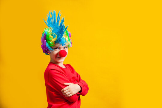 Boy clown with red nose and wig on a yellow background, portrait by belt, yellow background in the studio, copy of the holiday