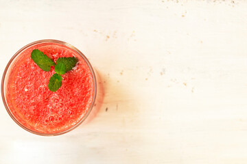 Delicious red watermelon juice with a sprig of green mint in a glass glass on a white background. Copy space. Summer food concept.