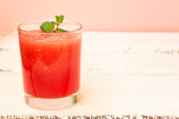 Delicious red watermelon juice with a sprig of green mint in a glass glass on a white background. Copy space. Summer food concept.