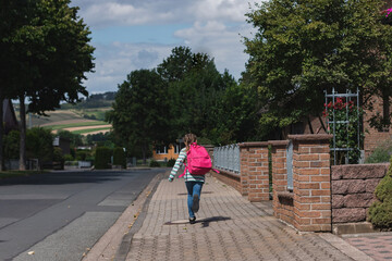 A girl with a pink satchel on her back runs down the street to school. The first day of school, the children are ready to study after the holidays.