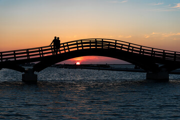 Naklejka na ściany i meble Wooden bridge in Lefkada at Sunset with two people silhoutted