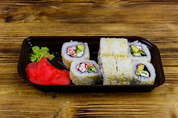 Uramaki sushi rolls with surimi in plastic box on wooden table. Sushi for take away or delivery of sushi in plastic container