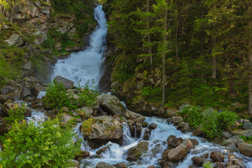 a deafening waterrfall falling from glaciers in the National Park of Great Paradise,in Piedmont,Italy. /an imposing waterfall flows impetuously in the midst of  alpine vegetation