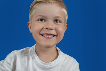 The happy smiling child looks straight and smiles on a blue plain background