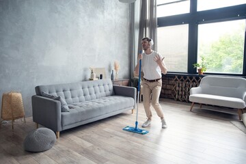 Young man having fun while cleaning his flat