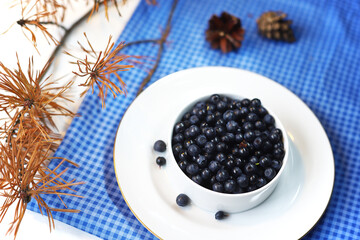 Blueberries on a white saucer on a checkered napkin decorated with a spruce branch and cones