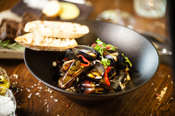 Blue mussels in white wine sauce in black bowl. Delicious healthy seafood closeup served on a table for lunch in modern cuisine gourmet restaurant