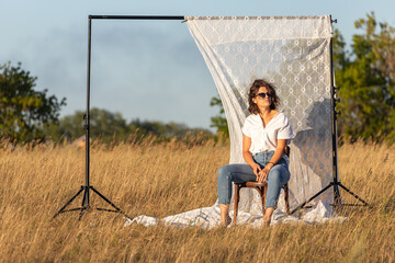 Atmospheric portrait of a young woman in  stylish clothers sitting on chair in nature. The concept...