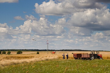 Ludzie na polu przy ciągniku rolniczym czekający na kombajn zbożowy - obrazy, fototapety, plakaty