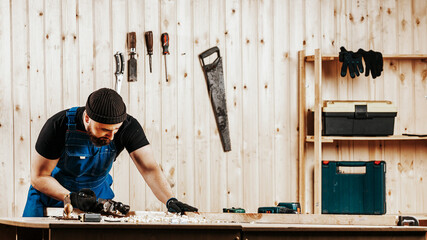 Close-up as a young  man by profession carpenter builder equals a wooden bar with a jack plane on a wooden table in the workshop