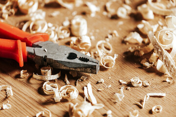A orange pliers  is on a wooden table, next to a wooden sawdust in the workshop