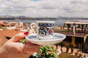 Traditional Turkish tea cup with ornaments in hands with the view of mosque in Istanbul