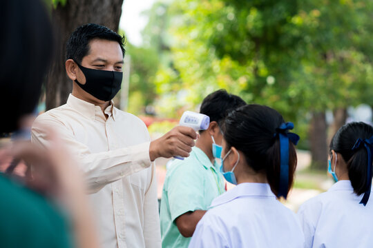 Teacher use infrared thermometer gun forehead temperature test to check student for protect virus covid-19 symptoms in the school
