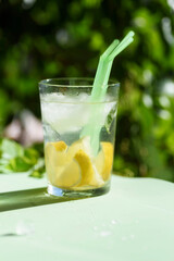 glass with refreshing drink with ice, lemon and straws, on a green background. Summer drink.