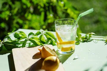 glass with refreshing drink with ice, lemon and straws, on a green background. Summer drink.
