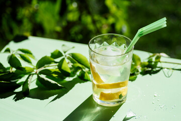 glass with refreshing drink with ice, lemon and straws, on a green background. Summer drink.