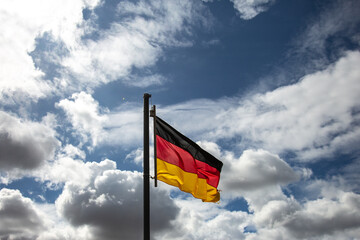 German flag on a flagstaff waving in the wind in front of a blue sky with white clouds