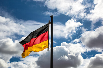 German flag on a flagstaff waving in the wind in front of a blue sky with white clouds