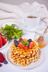 Plate with sweet tasty waffles with honey, berries, cup of tea on the white background.