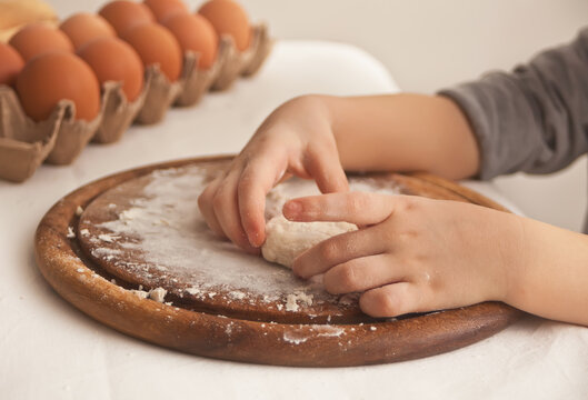 Little child in the home kitchen preparing dough for pizza or another food.