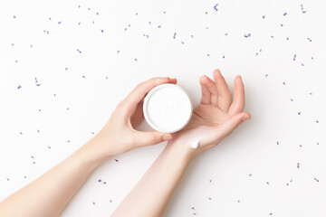 Beautiful well-conditioned female hands moisturizing cream surrounded with lavender flowers on the white background. Hand and body care concept