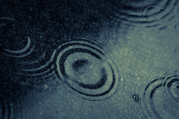 A close up of rain drops landing on a sidewalk forming concentric circles.