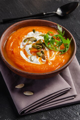 Tasty homemade rustic pumpkin soup with seeds in clay dish on slate tray