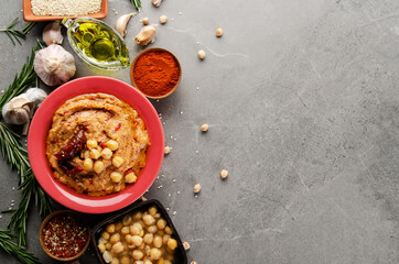 Hummus topped with chickpeas, olive oil, green coriander leaves and sun dried tomatoes on stone table with pita bread and spices aside. Flat lay