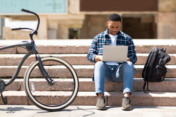 Student using laptop, sitting on the steps in city