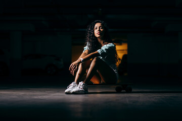 Beautiful afro american  girl sitting on a skateboard in the underground Parking