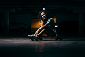 Fototapeta na wymiar Beautiful afro american girl sitting on a skateboard in the underground Parking