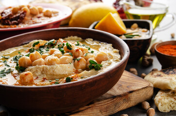 Fresh homemade Hummus in clay dish topped with olive oil, chickpeas and chopped green coriander leaves on stone table served with spices