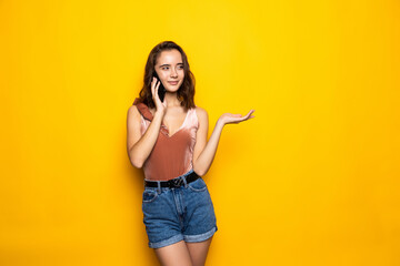 Charming surprised young woman talking on cell phone over yellow background